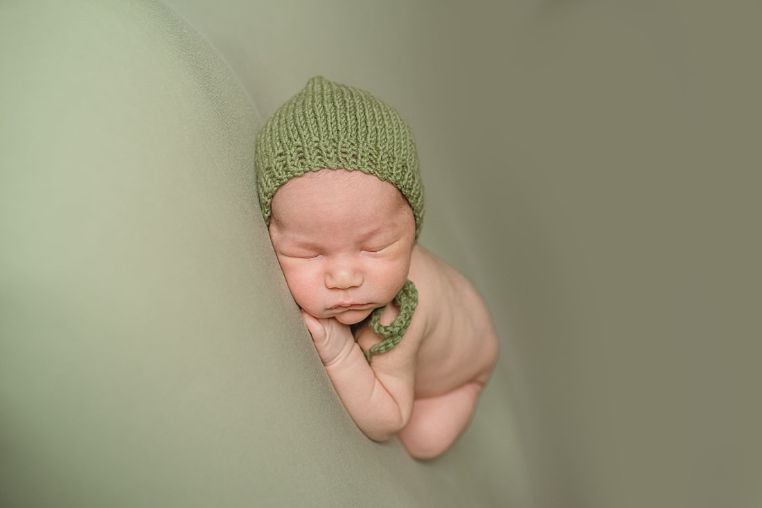 adorable newborn baby boy wearing green bonnet during newborn photo shoot