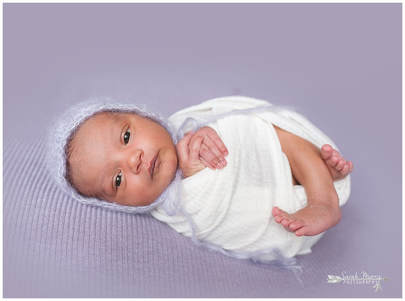 newborn photos of baby girl on purple blanket wearing a bonnet