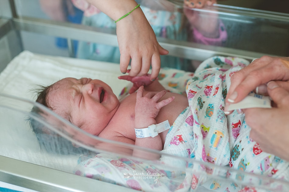 big sister holds newborn baby sister's hand as the pediatric nurse checks her vitals at Methodist Le Bonheur Germantown Hospital