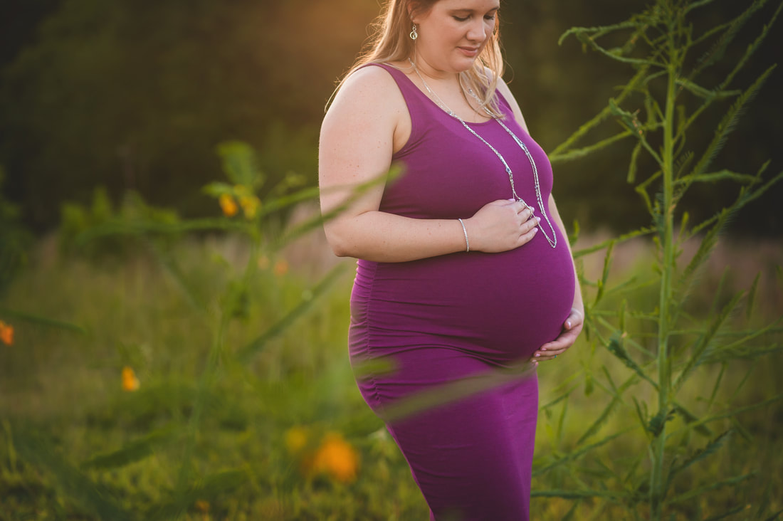 pregnant mother holding her belly in the tall grasses at Shelby Farms Park in Memphis, TN