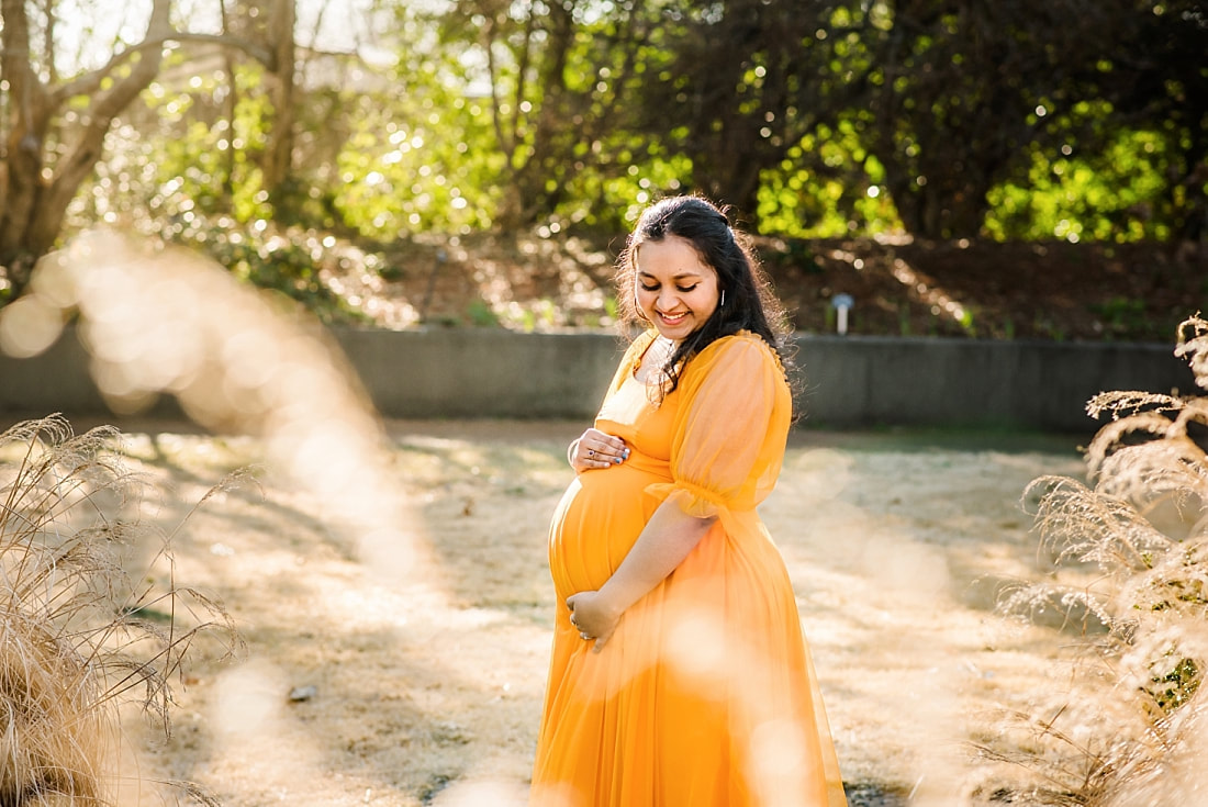 beautiful pregnant mother looks down at her belly at memphis botanic garden