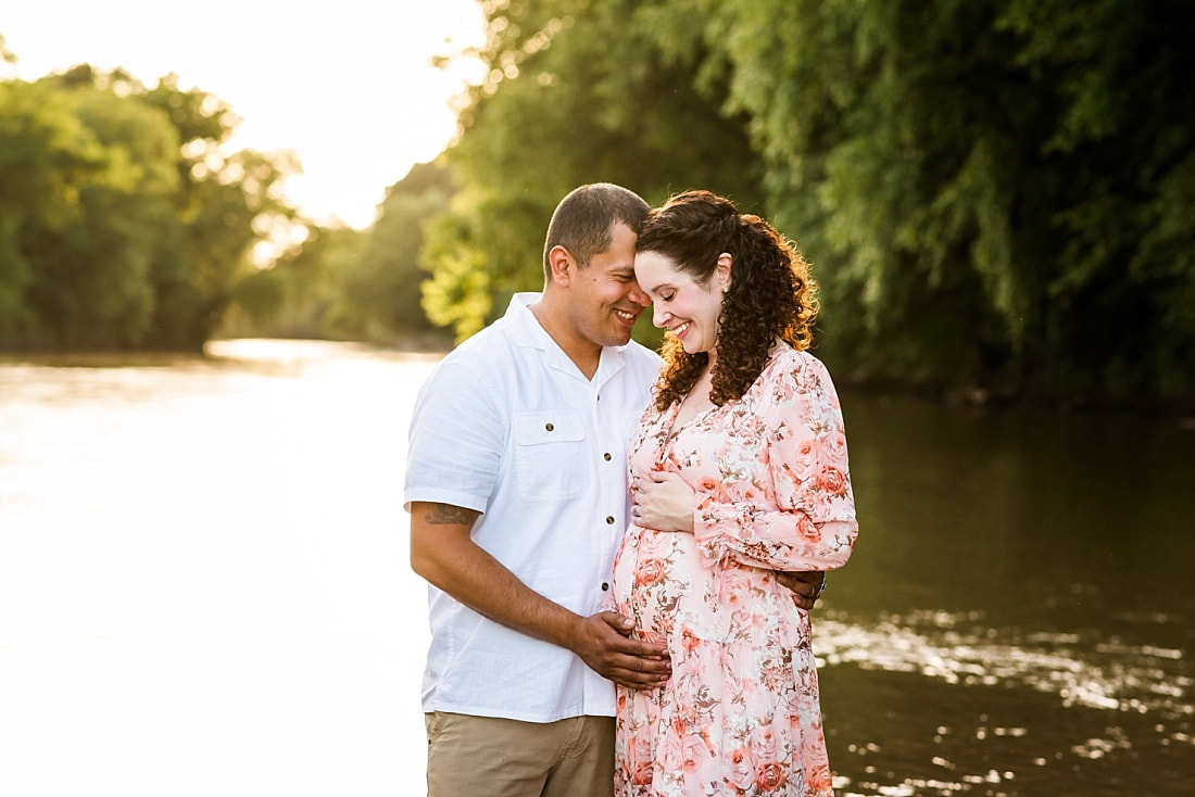 mother and father embracing pregnant belly at the creek in Memphis, TN