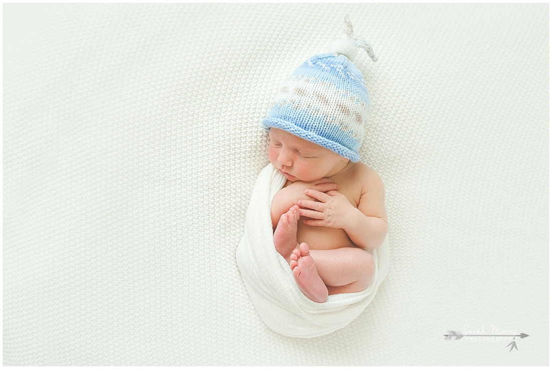 Newborn photo of baby boy sleeping on white blanket wearing blue hat