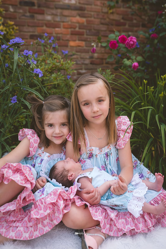 Big sisters holding their newborn baby sister in the flowers