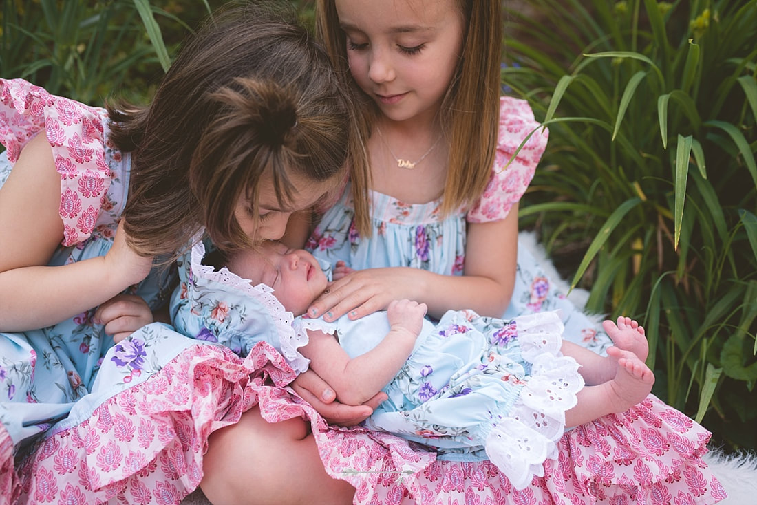 Big sisters holding their newborn baby sister in the flowers