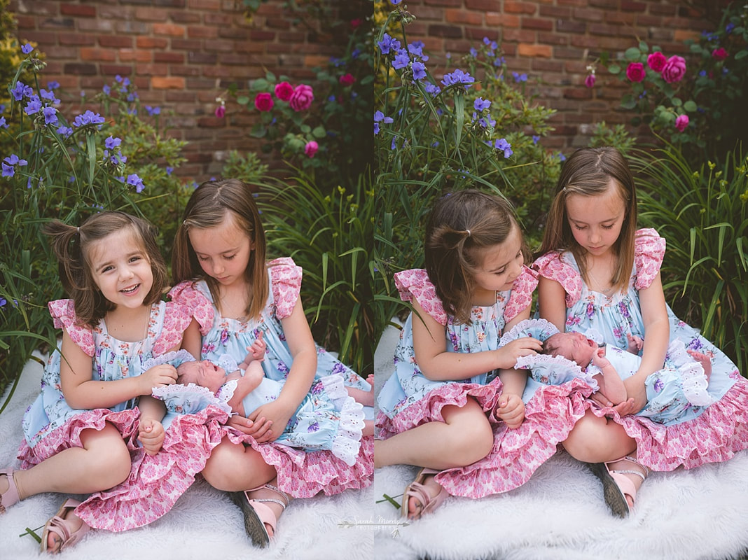 Big sisters holding their newborn baby sister in the flowers