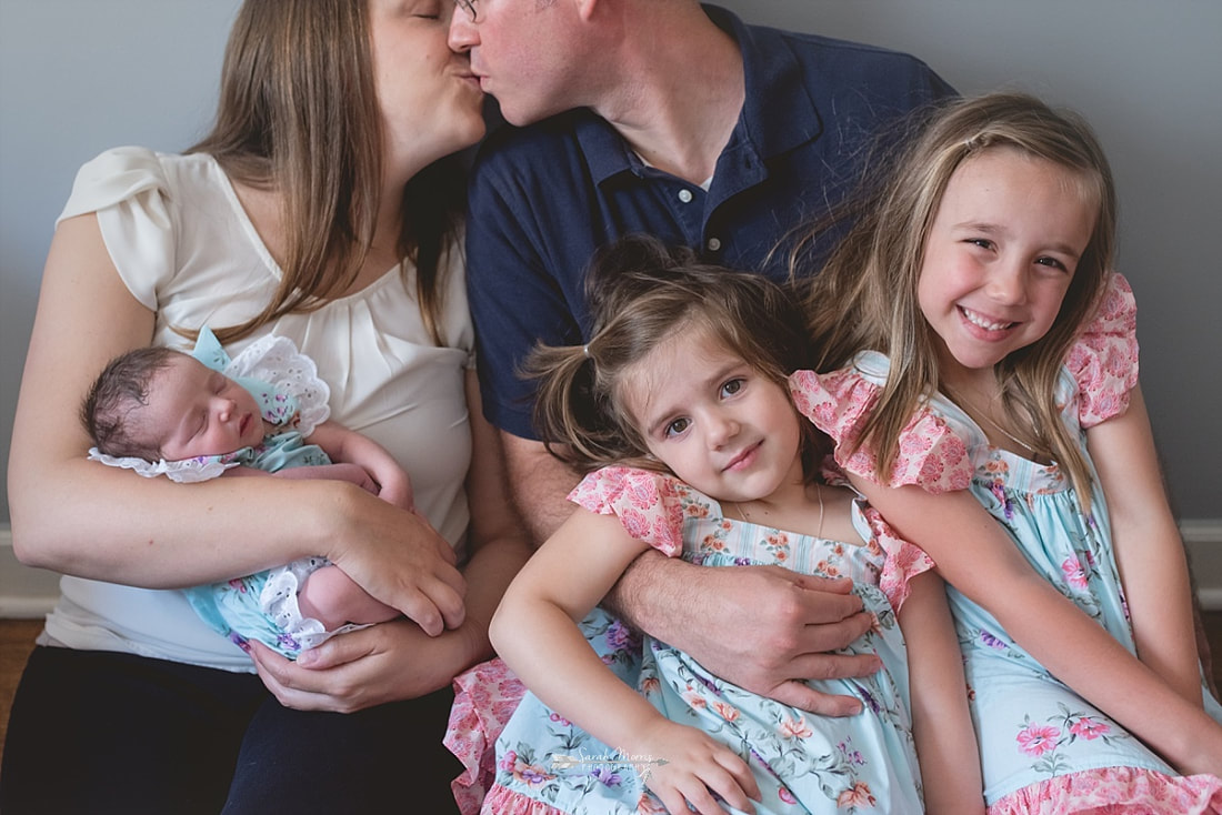 close up of all 3 girls while mom and dad kiss in the background at baby sister's newborn session
