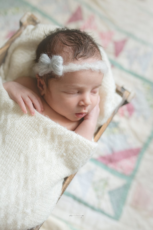 newborn baby girl wearing a bow, wrapped in a cream blanket, sleeping in a rustic wooden box on top of a vintage quilt
