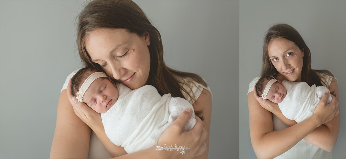Mother holding her newborn baby girl close to her face while she's swaddled in a cream blanket