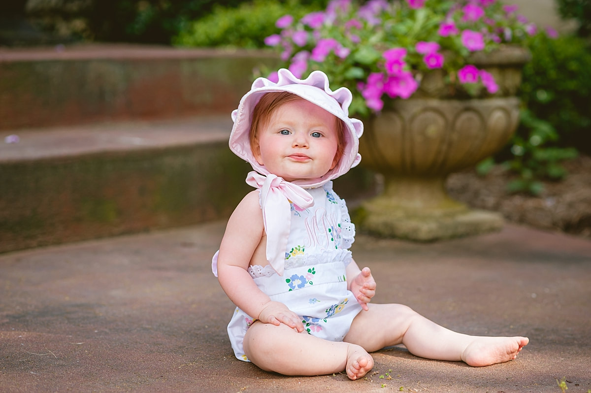 baby girl's first birthday portrait, wearing a monogrammed bubble and Beaufort bonnet on the front porch during in home lifestyle family session in collierville, tn