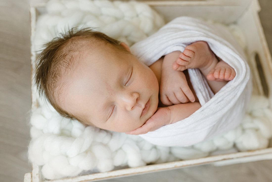 baby girl swaddled in white blanket, sleeping in basket for newborn photos in Memphis, TN