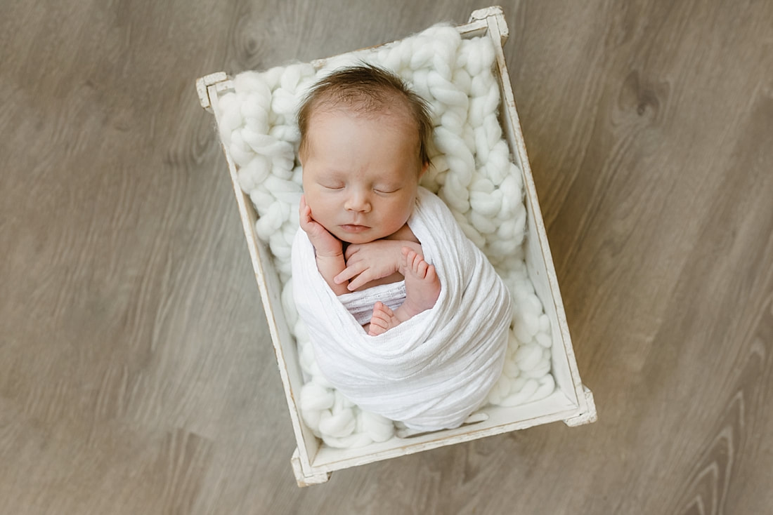 baby girl swaddled in white blanket, sleeping in basket for newborn photos in Memphis, TN