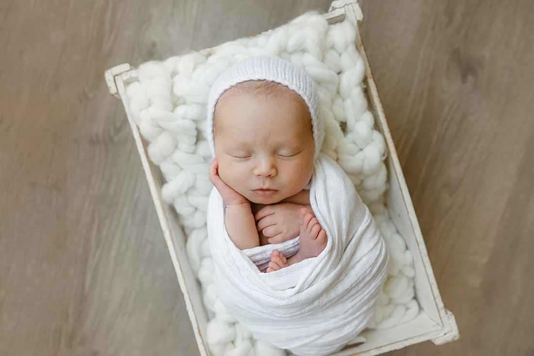 baby girl swaddled in white blanket, sleeping in basket for newborn photos in Memphis, TN