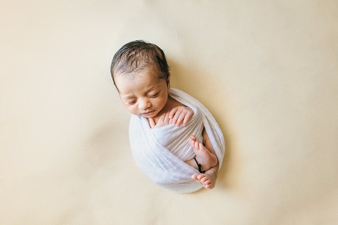 newborn baby wrapped in white on yellow background for newborn photos in memphis