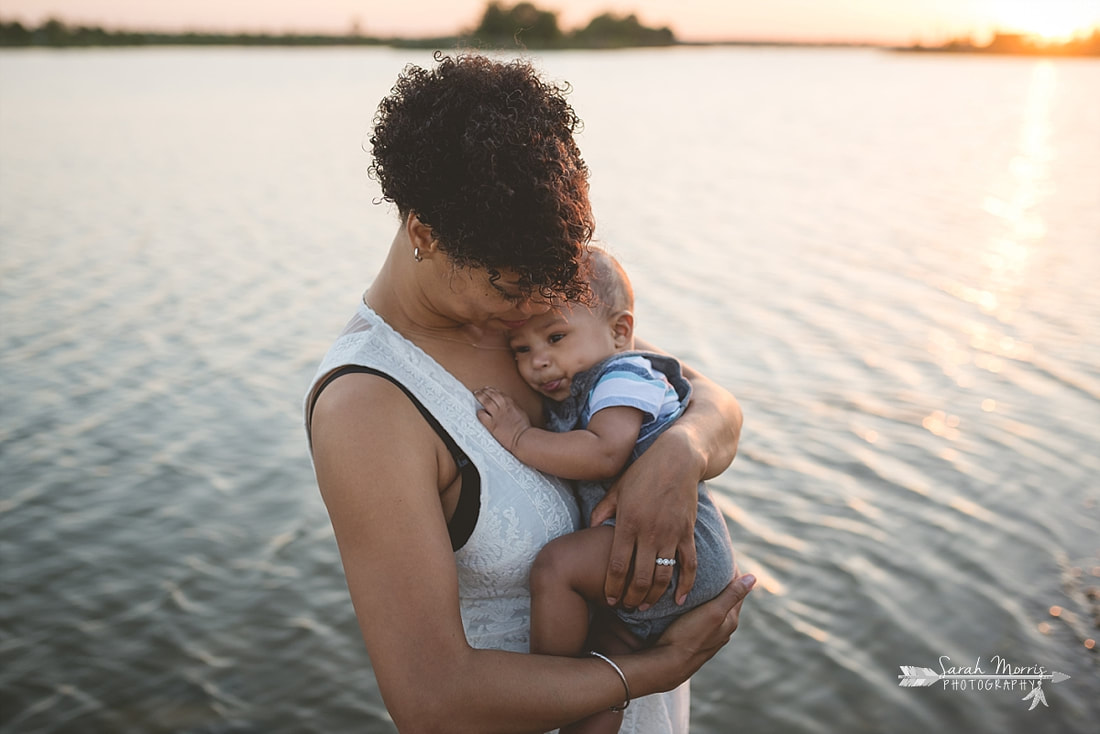 Mother holding baby on the bank of Patriot Lake at sunset at Shelby Farms Park