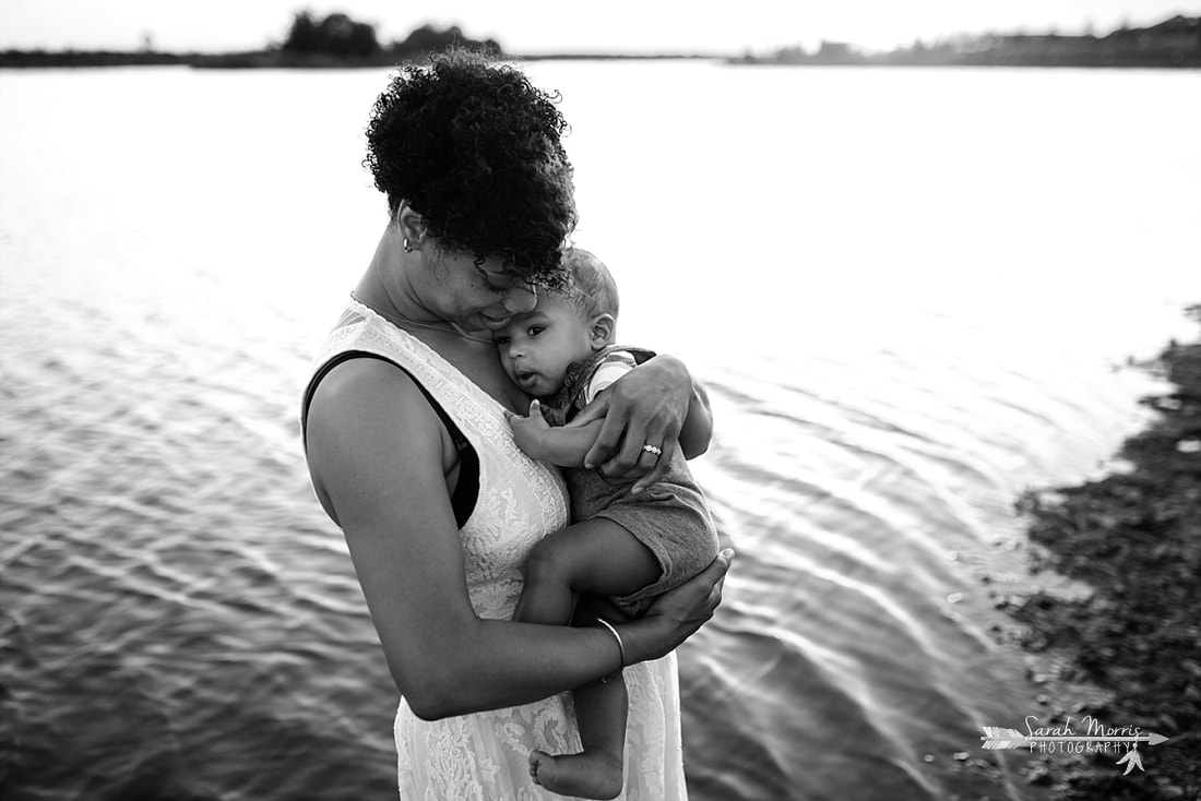 Mother holding baby on the bank of Patriot Lake at sunset at Shelby Farms Park