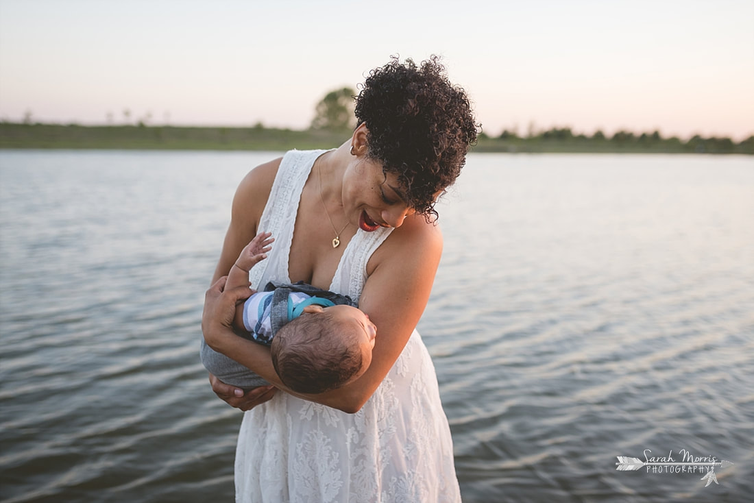 Mother holding baby on the bank of Patriot Lake at sunset at Shelby Farms Park