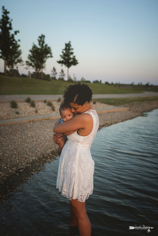 Mother holding baby on the bank of Patriot Lake at sunset at Shelby Farms Park