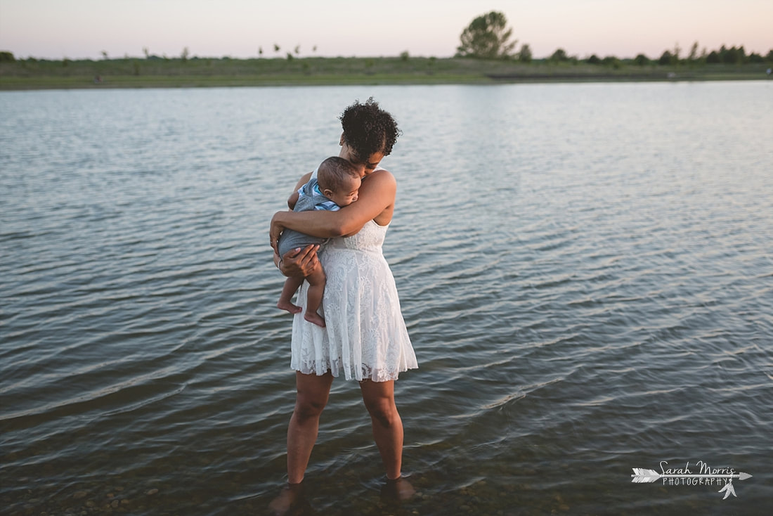 Mother holding baby on the bank of Patriot Lake at sunset at Shelby Farms Park