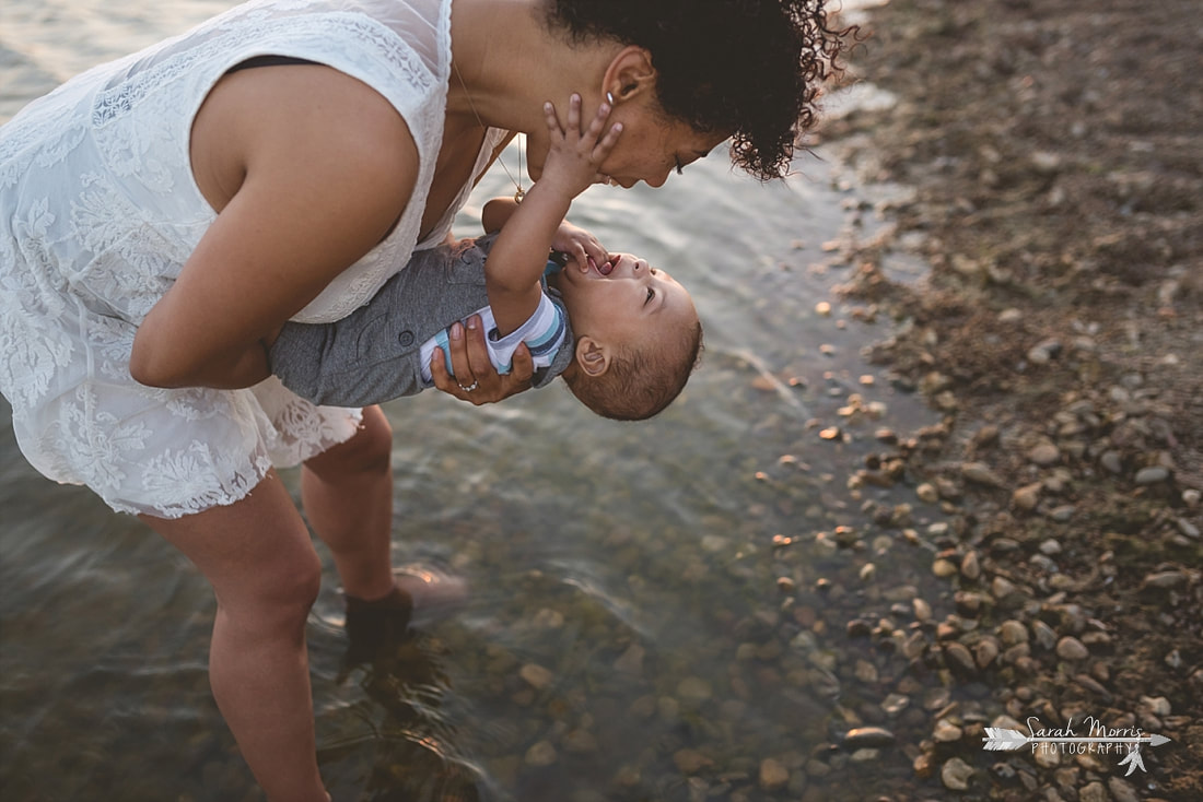 Mother holding baby on the bank of Patriot Lake at sunset at Shelby Farms Park