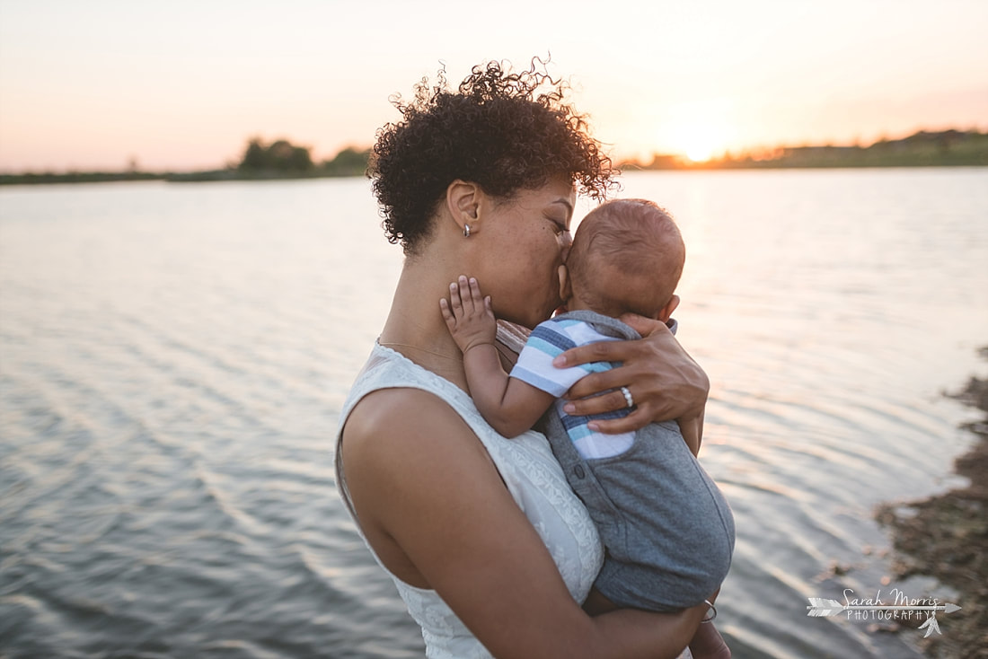 Mother holding baby on the bank of Patriot Lake at sunset at Shelby Farms Park