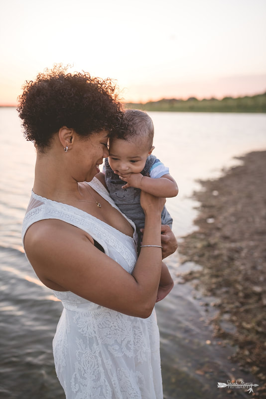 Mother holding baby on the bank of Patriot Lake at sunset at Shelby Farms Park